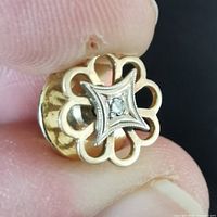 Close-up photo of the gold and diamond pin brooch held between fingers. Shows intricate open petal design and the diamond centerpiece in silver-toned setting.