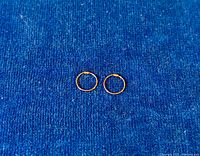 Pair of small gold hoop earrings placed on a blue fabric background showing overall appearance and size of the earrings.