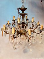 Full view of the antique brass chandelier showing multiple arms with candle-style socket holders and hanging crystal prisms.