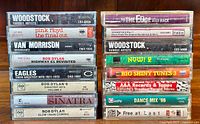 Stack of 14 vintage cassette tapes in original plastic cases showing spine titles including Woodstock, Pink Floyd The Final Cut, Van Morrison Moondance, Bob Dylan, Eagles, Frank Sinatra, and various compilation albums.