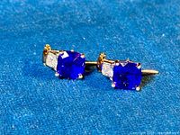 Close-up photo of the pair of piercing stud earrings with deep blue sapphire CZ stones set in gold washed sterling silver, showing the front and detail of stones and metal.