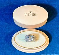 Ring with large cushion-cut cubic zirconia set in 925 sterling silver with decorative accent stones displayed in oval jewelry box.