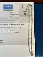 Appraisal certificate page showing chain and pendant laid on blue surface