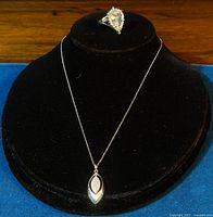 Front view of ring and pendant necklace displayed on black jewelry stand showing pendant with inset CZ stones and ring with pear-shaped CZ center and halo.