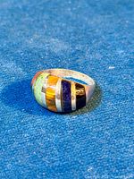 Chunky dome-shaped ring with colorful semi-precious stone inlays lying flat on blue textured surface