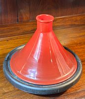 Red stoneware cone-shaped lid of the Le Creuset Tagine on wooden surface showing smooth glazed finish.
