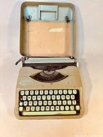 Typewriter open in upper case half showing keyboard, front panel inscription, platen and carriage