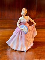 Front view of Royal Doulton figurine showing a woman in pink gown holding a blue floral fan.