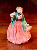 Full front view of the Royal Doulton Lady Charmian figurine in red dress and green shawl holding flowers and basket.