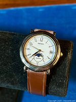 Front-angle view of watch on display stand showing dial, moonphase and date.