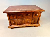 Front view of vintage solid wood apothecary cabinet showing 8 small drawers with wooden knobs