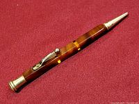 Full view of the vintage pencil showing brown marbled Bakelite body, silver metal tip, and clip on crimson background.