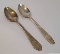 Two silver spoons showing front side with engraved handles and smooth bowls