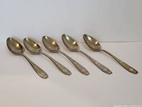 Side view of five Arabic silver spoons laid side by side showing shape and handle decoration