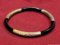 Top view of the circular bangle bracelet showing alternating black and gold tone metal sections with engraved floral designs.