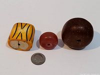 Three antique necklace stones with a coin for scale: a large brown round bead, a medium red bead, and a yellow rectangular bead with black patterns.