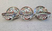 Front view of three teacups with matching saucers behind, showing colorful bird and floral decorations on shell-shaped ceramic cups.
