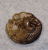 Top view close-up of the circular carved jade pendant showing detailed scales and creature's head.