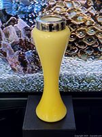 Antique citron yellow glass vase with sterling silver collar on a dark platform, showing overall shape and color against a patterned background.
