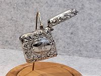 Close-up image of antique silver matchbox with ornate scrolling and monogram visible on the front, lid open.