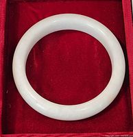 Top-down view of the circular white jade bangle bracelet in a red box, showing the smooth surface and uniform color.