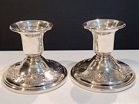 Pair of Birks sterling silver candlesticks shown side by side on white surface against black background