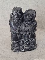Front view of vintage Inuit stone carving showing two figures in traditional attire embracing each other.