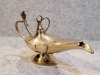 Front angle view of the small brass oil lamp showing the spout, hinged lid, and pedestal base