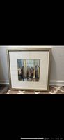 Framed abstract cityscape painting with muted tones and textured appearance inside a beige frame and white mat.