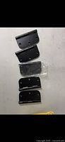 Photo showing five black metal door hinges arranged vertically on a light surface. One hinge is still wrapped in clear plastic.