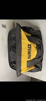 Closed DeWalt yellow and black soft tool bag with handles lying flat on white surface.