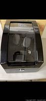 Closed black automatic watch winder box with transparent top window under natural lighting.