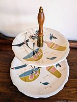 Photo of the assembled two-tiered vintage ceramic serving tray from above, showing the hand-painted abstract designs on the scalloped plates and wooden handle.