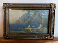 Front view of antique scenic print in wooden frame showing two figures by a lake with mountain background.