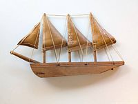Front view of the wooden sailboat model showing the three masts and birch bark sails hung with string rigging on the wood hull base.