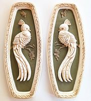 Front view of two vintage chalkware plaques depicting white peacocks on olive green backgrounds with cream borders.