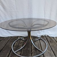 Front angled view of side table showing round glass top and curved chrome metal base.