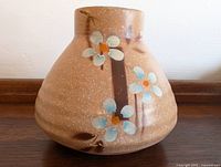 Side view of brown pottery vase with hand-painted blue and white flowers and orange centers, speckled surface.