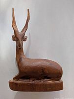 Front view of the carved wooden antelope sculpture showing detailed facial features and elongated horns, seated on a round base.