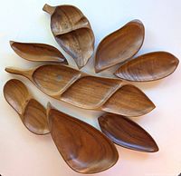 Top view of eight Monkey Pod wood serving bowls in various leaf shapes arranged on a white background showing wood grain and natural coloration.