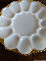 Top view of milk glass egg plate showing 12 egg-shaped compartments and gold scalloped rim.