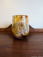 Front view of the amber-yellow-brown blended Murano glass vase on a wooden surface against a white background.