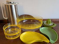 Full patio serving lot showing thermos, glass bowls with yellow stripes, green and yellow speckled dishes, and green glass juicer