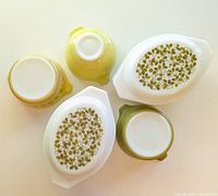 Top view of two white casseroles with olive green leaf pattern lids and three yellow/green bowls, showing designs and bottoms.