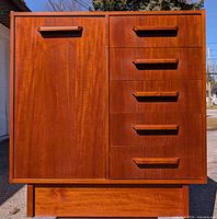 Front view of teak chest showing one door on left and five drawers on right with teak recessed handles.