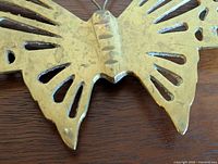 Close-up of one brass butterfly showing detailed cutout wings, solid ridged body and slight tarnishing.