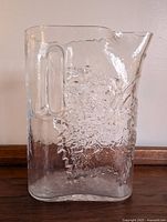 Front view of the clear glass pitcher showing the embossed grapevine pattern and integrated handle.
