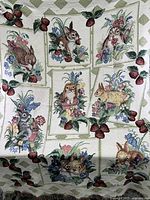Woven cotton tapestry throw laid out showing embroidered panels with rabbits, owl, flowers, and strawberries inside framed rectangles with green diamond background pattern.