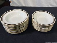 Two stacks of Aynsley South Pacific bone china bowls, the left stack taller with larger bowls and the right stack smaller bowls, showing gold rims and black and white pattern.