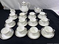 Full tea set composition showing teapot, sugar bowl, creamer, six cups and six saucers on black background.